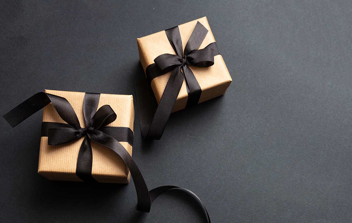 Last Minute Holiday Gifts Two gold colored gift boxes with black bows on a black background.