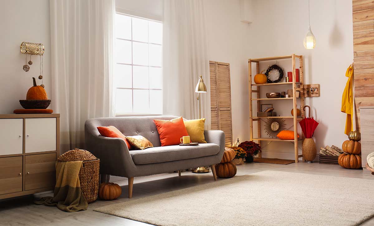 Transitioning Your Apartment from Fall to Winter Fall decorated apartment with pumpkins and orange colored pillows on gray couch.