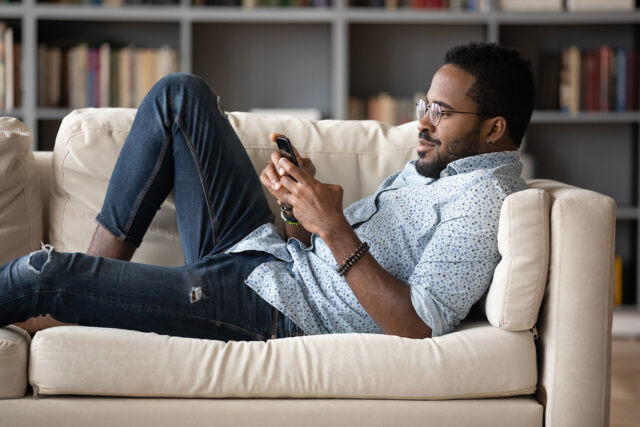 Guy on couch playing game on his smart phone.