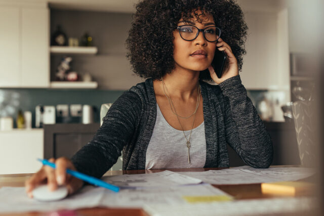 Woman with black curly hair, working from home on the phone and computer.