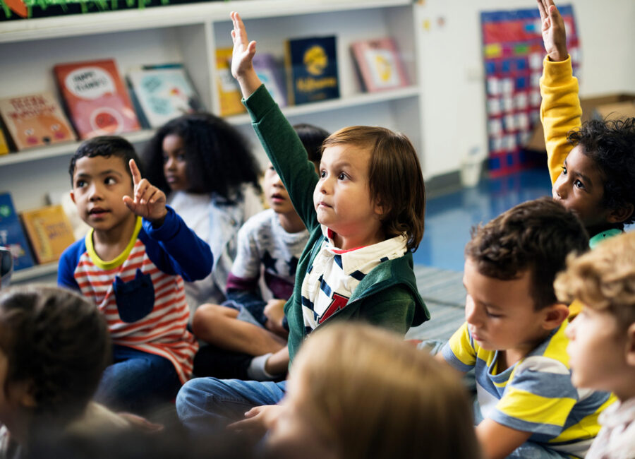 Group of elementary students with one child's hand raised.